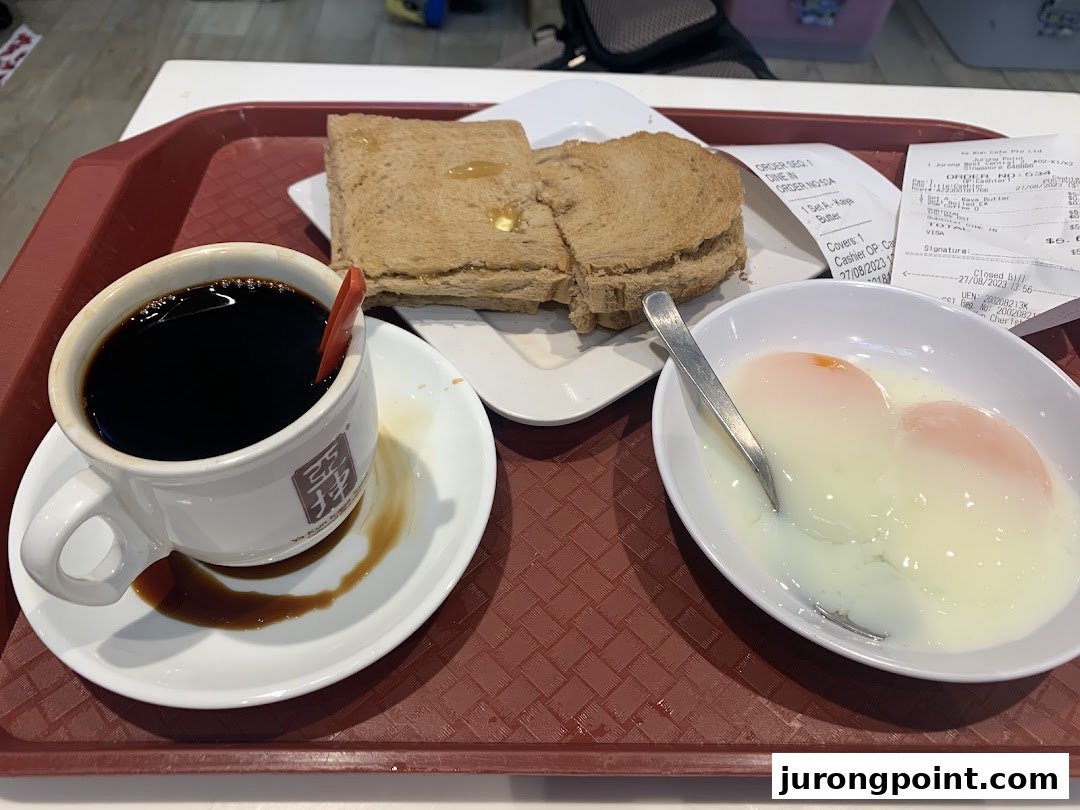 A traditional Singaporean breakfast set featuring coffee, kaya toast, and soft-boiled eggs on a tray.