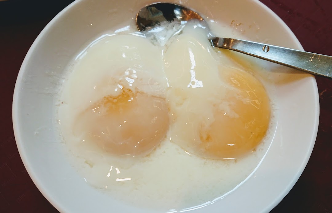 A close-up of two perfectly cooked soft-boiled eggs in a white bowl with a spoon.