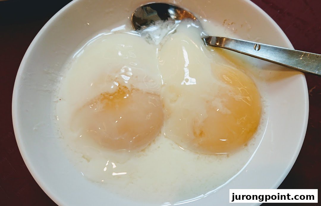 A close-up of two perfectly cooked soft-boiled eggs in a white bowl with a spoon.