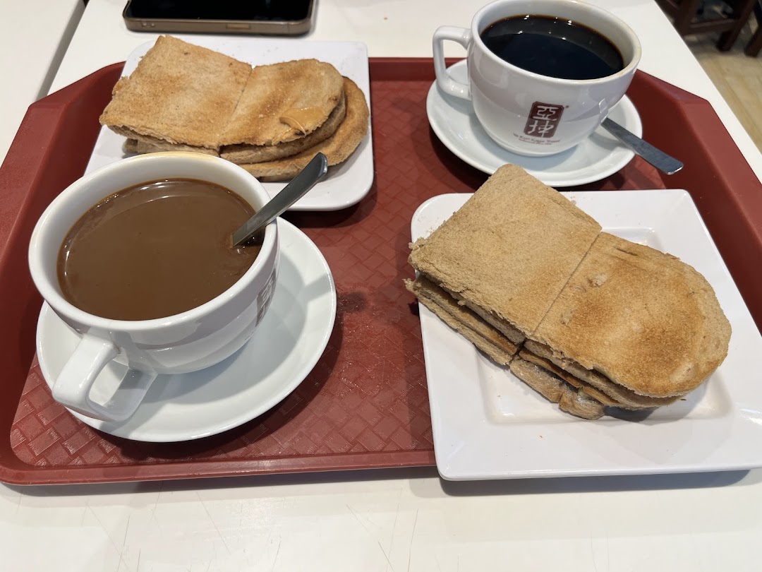 A classic Singaporean breakfast set featuring kaya toast and two cups of coffee/tea on a red tray.