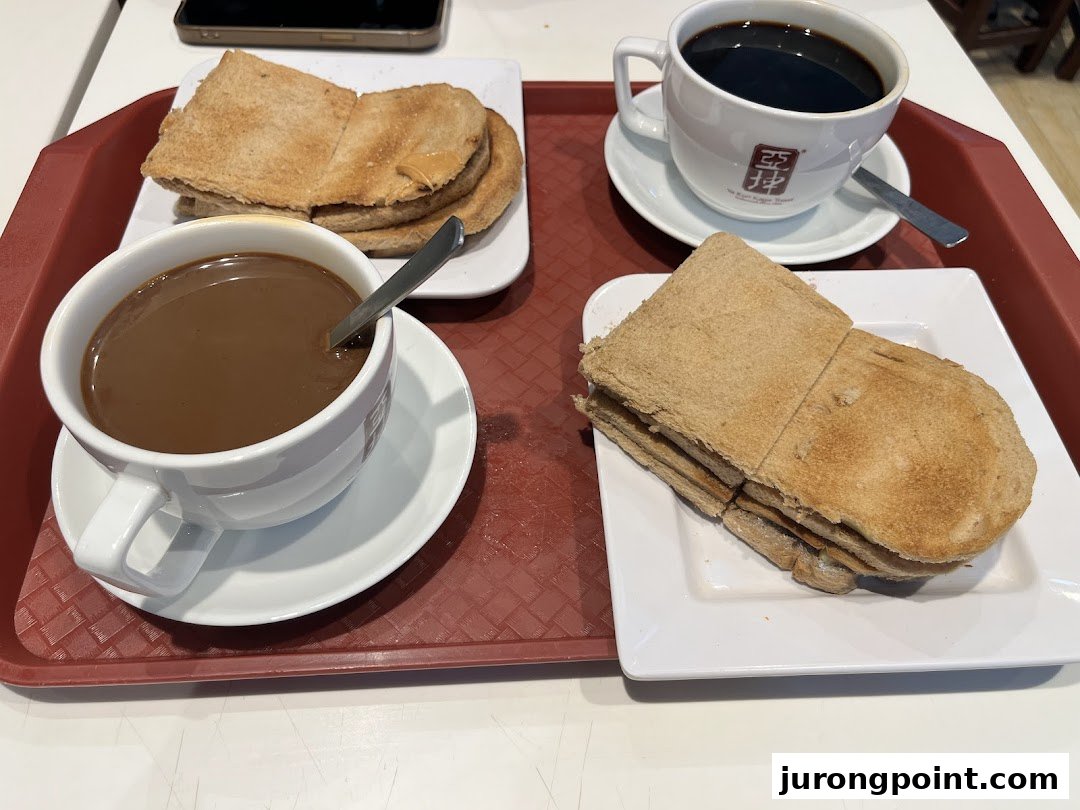 A classic Singaporean breakfast set featuring kaya toast and two cups of coffee/tea on a red tray.
