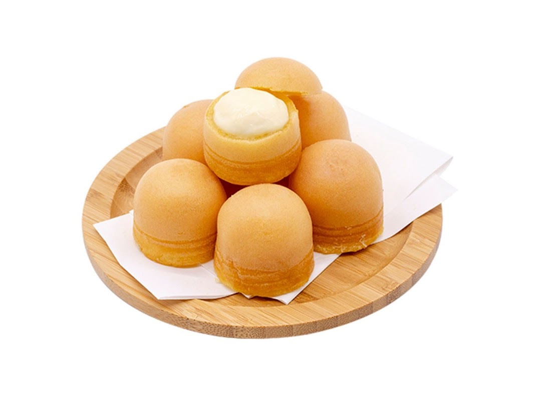 A wooden plate holds several golden-brown, dome-shaped pastries, one revealing a creamy white filling.
