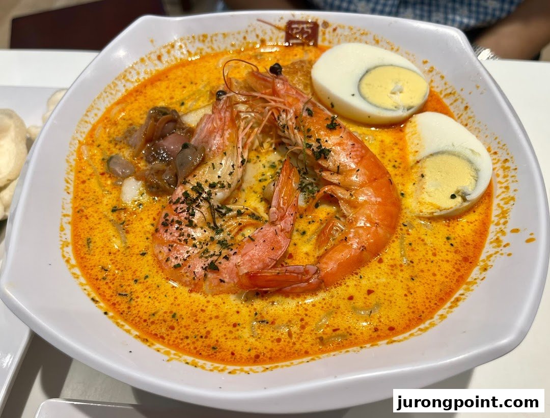 A vibrant bowl of spicy noodle soup with large prawns, clams, and hard-boiled eggs.