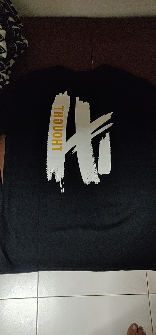 A black t-shirt featuring a white brushstroke design and the word 'THOUGHT' in gold.