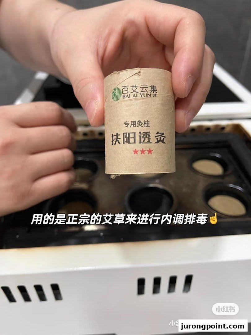 A hand holds a moxa stick over a moxibustion device, highlighting a TCM treatment.