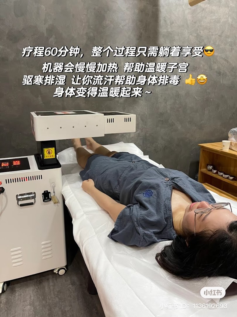 A person lies on a treatment bed receiving a warming therapy at a TCM clinic.
