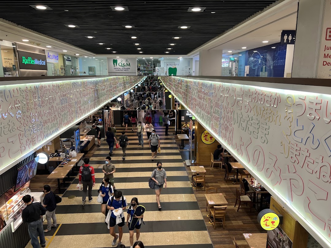 A bustling mall interior with multiple levels, shops, and eateries, featuring a decorative wall.