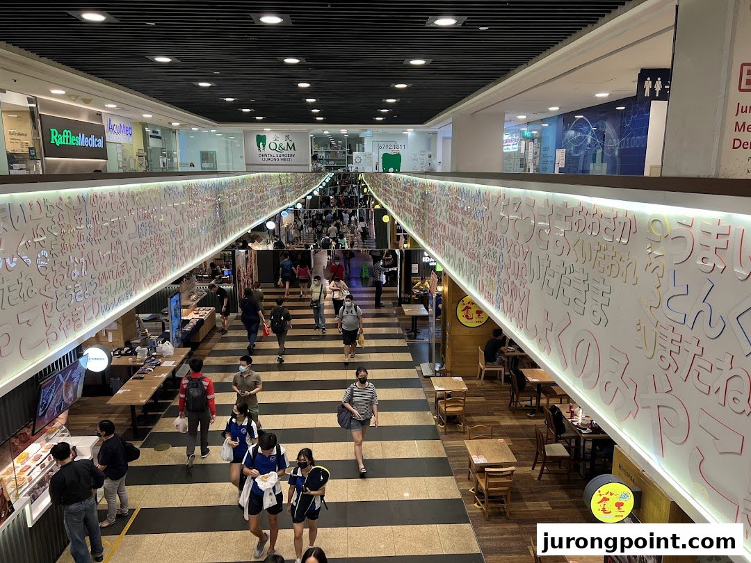 A bustling mall interior with multiple levels, shops, and eateries, featuring a decorative wall.