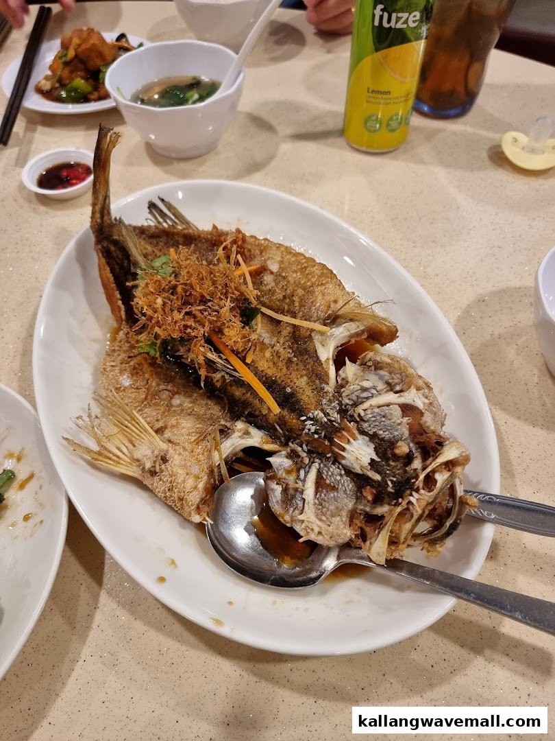 A beautifully presented fried fish dish, garnished with herbs, served on a white plate at a restaurant table.
