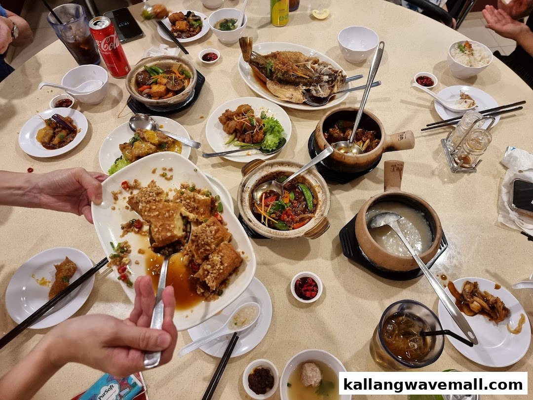 A table laden with various Chinese dishes, claypot meals, and drinks, with people dining.