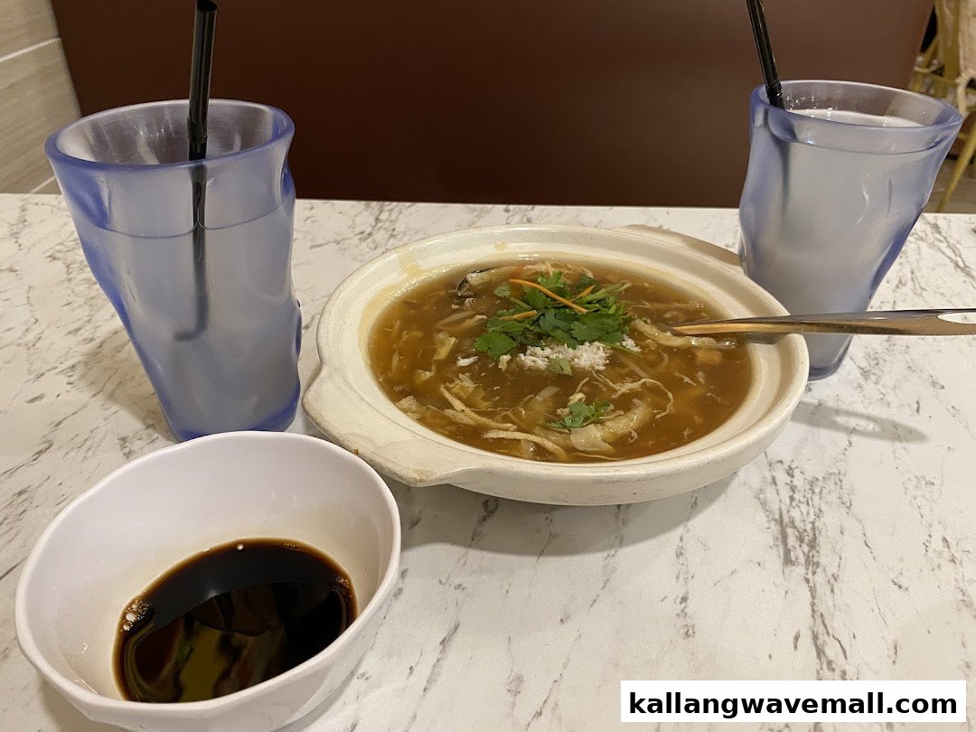 A hearty bowl of soup, two drinks, and a dipping sauce on a marble table.