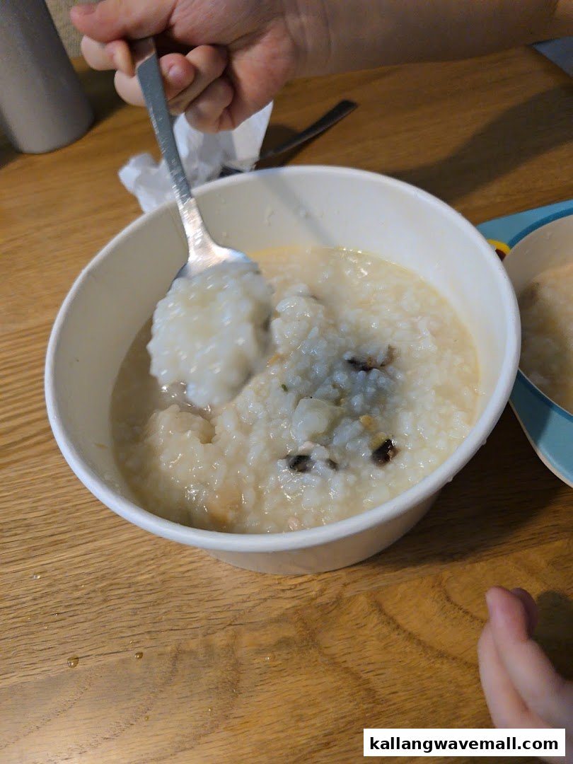 A hand spoons a serving of warm, savory porridge from a white bowl on a wooden table.