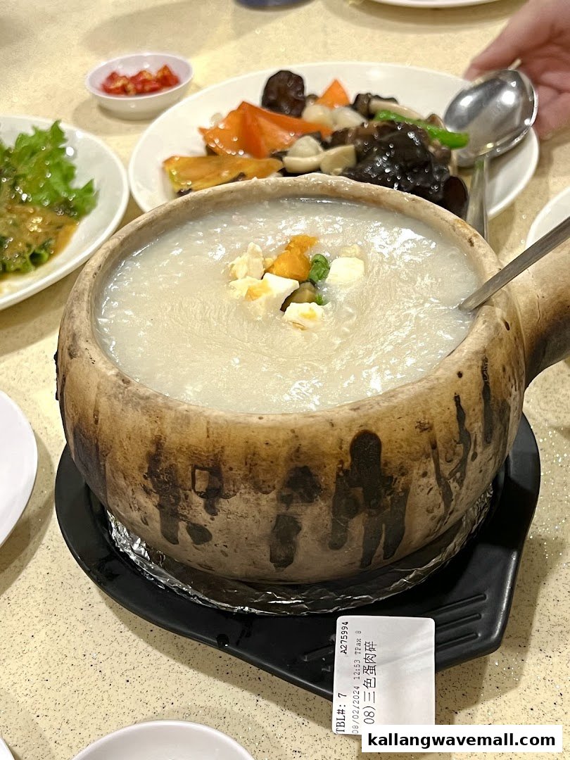 A steaming claypot of porridge topped with eggs, served with side dishes on a table.