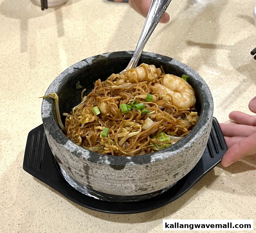 A hot stone bowl of stir-fried noodles with shrimp and vegetables, served at A1 Porridge.