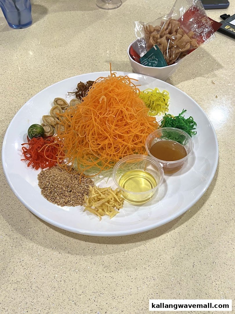 A vibrant Yu Sheng dish with shredded vegetables, nuts, sauces, and abalone on a white plate.