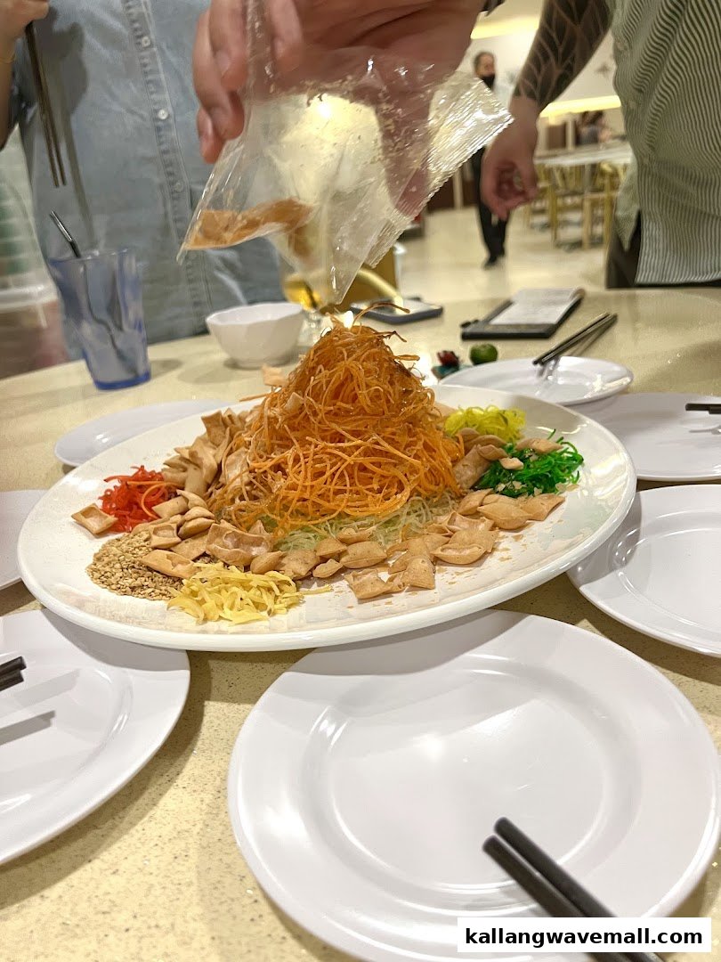 A large plate of colorful Yu Sheng (Lo Hei) being prepared at a table, surrounded by diners.