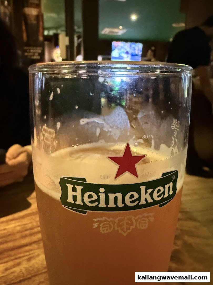 A close-up of a Heineken beer glass on a wooden table inside a dimly lit bar.