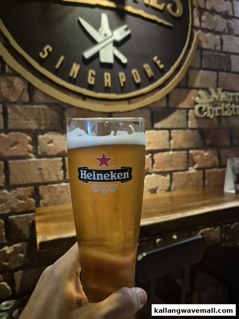 A hand holds a refreshing Heineken beer glass inside Al Capones, featuring a brick wall and the Singapore logo.