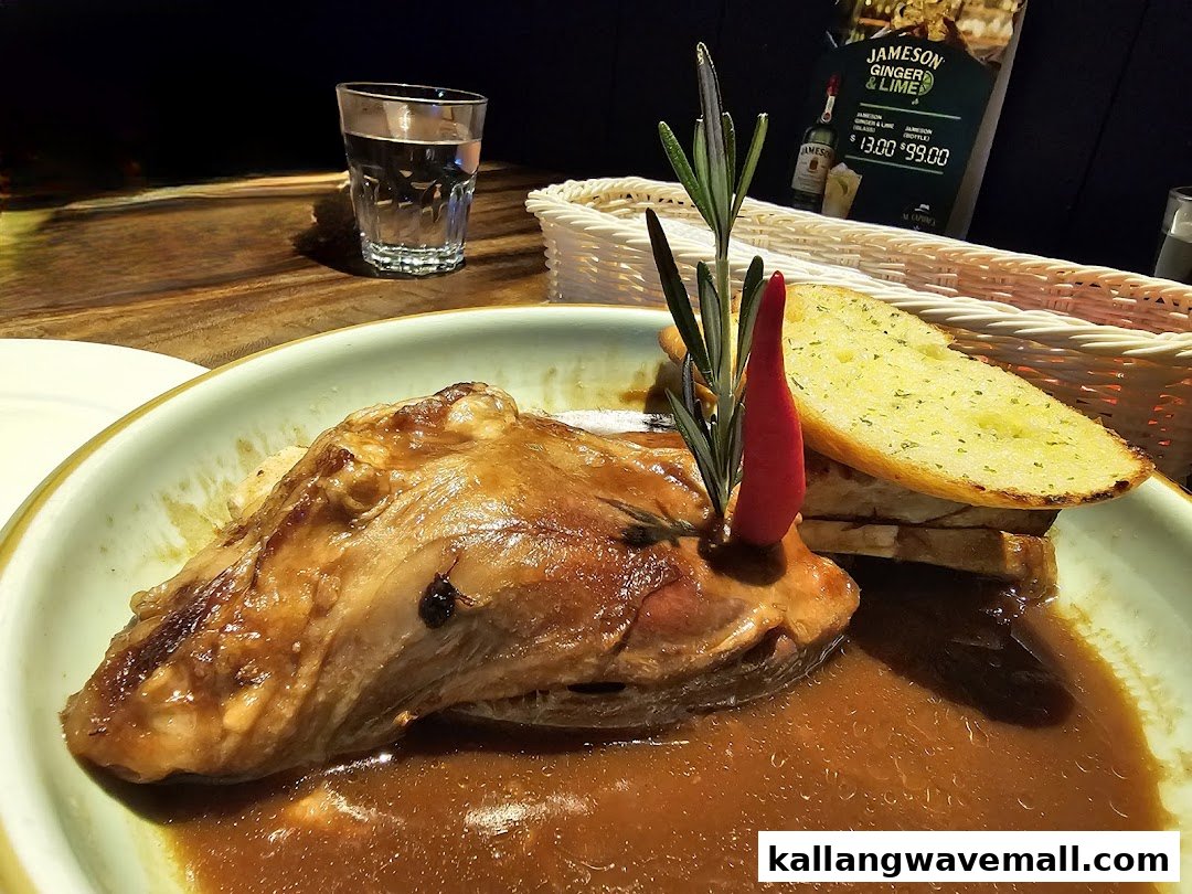 A close-up of a braised meat dish with garlic bread and a drink on a table at Al Capones.
