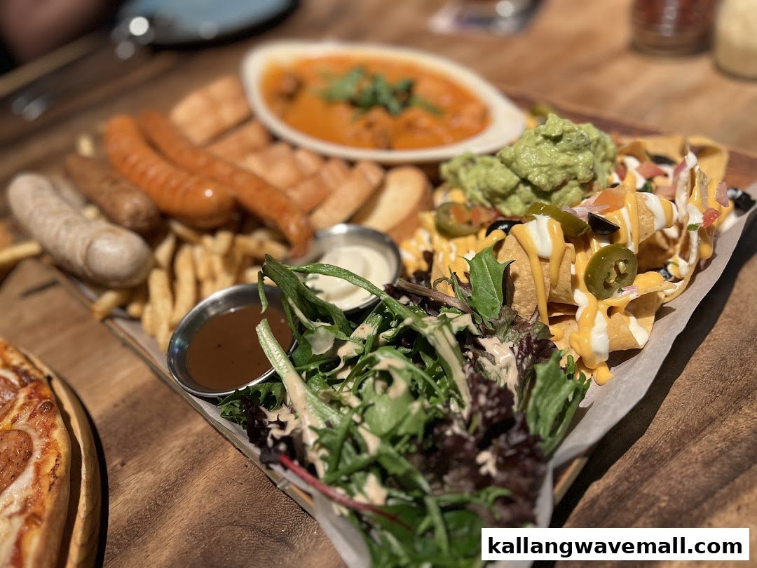 A delicious platter featuring sausages, fries, nachos with guacamole, and a fresh side salad.