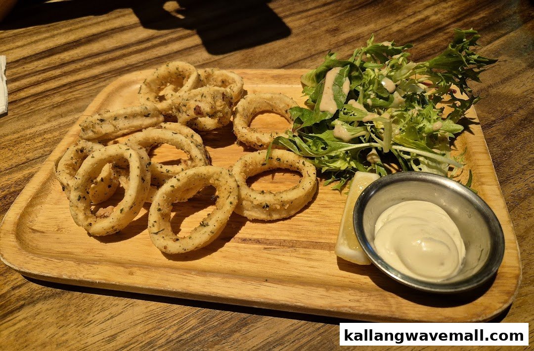A wooden platter featuring crispy calamari rings, fresh green salad with dressing, lemon wedge, and a side of dipping sauce.