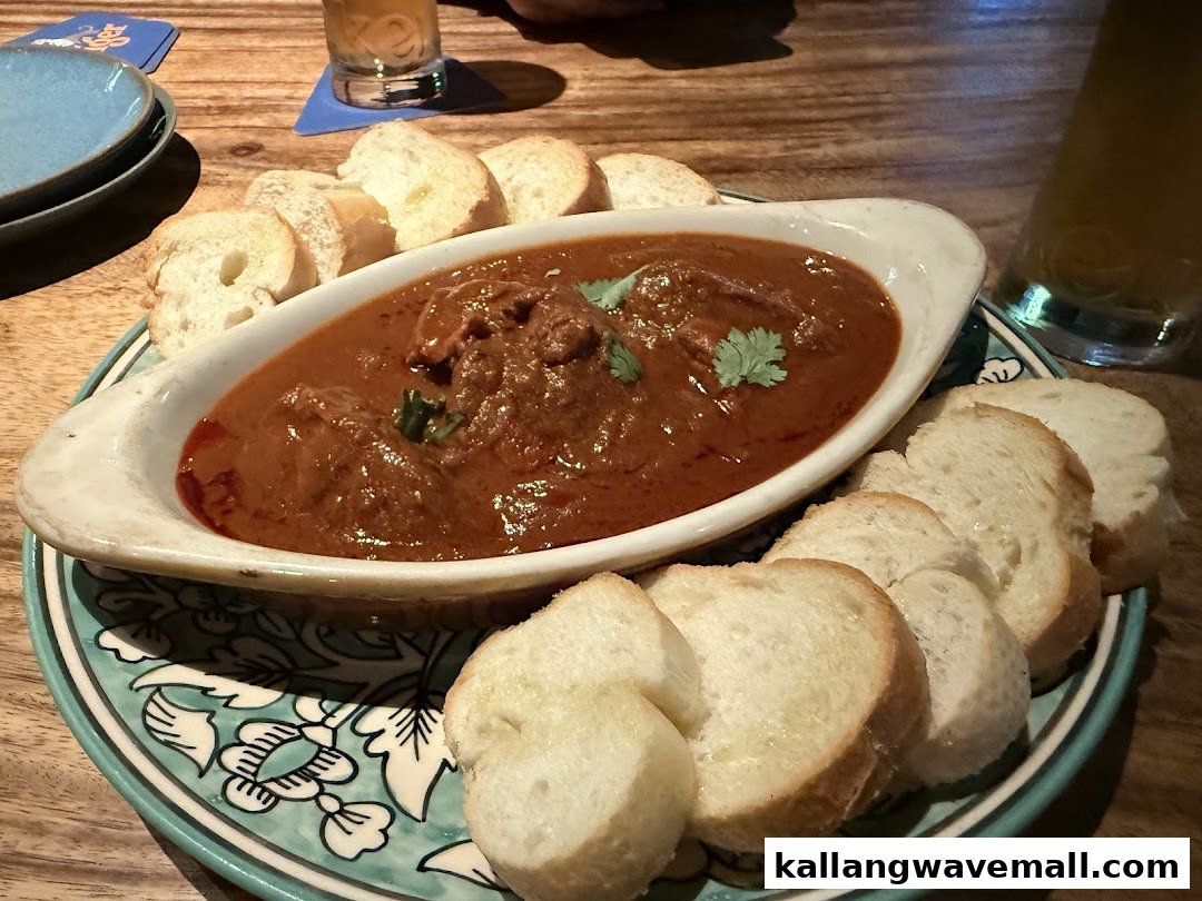 A rich, savory stew or curry with meat and fresh bread slices on a decorative plate.