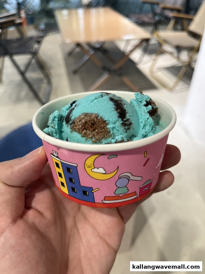 A hand holds a cup of vibrant blue ice cream with chocolate cookie pieces.