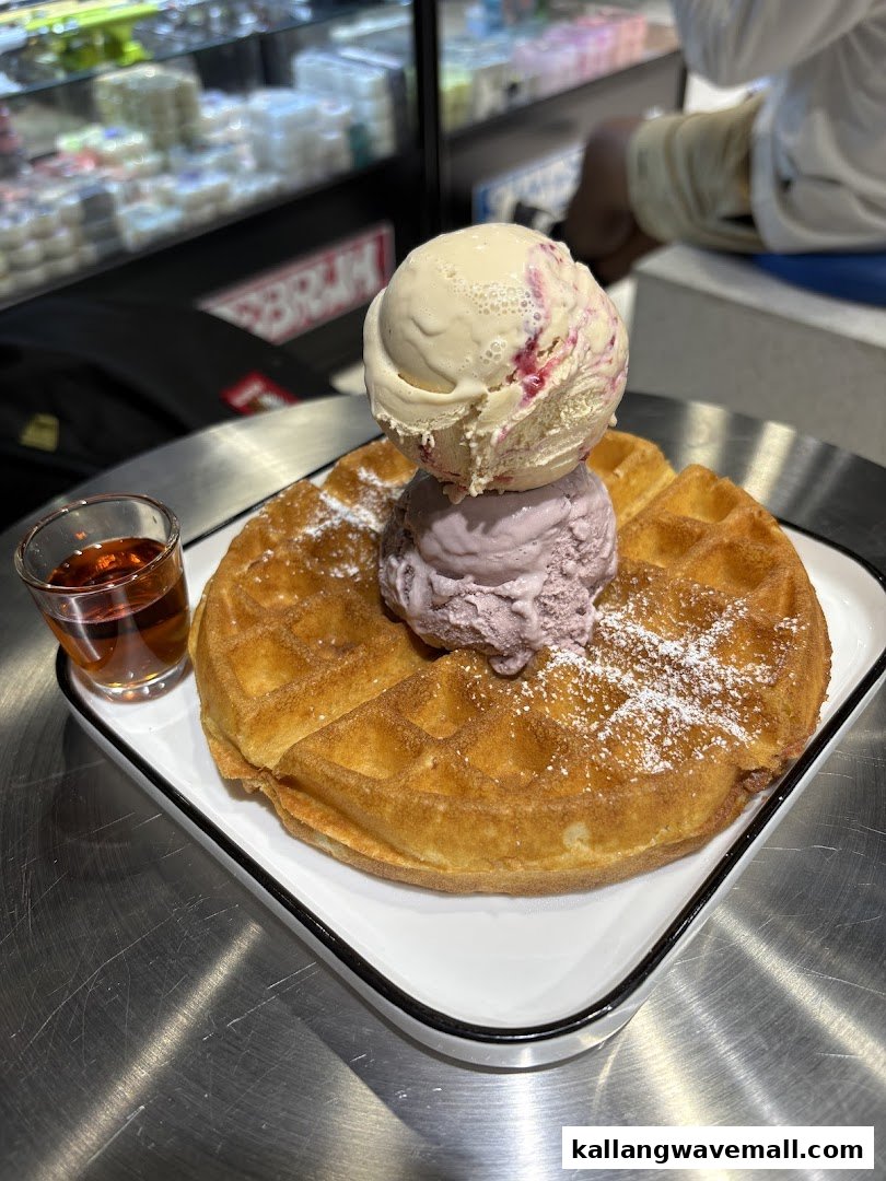 A golden waffle topped with two scoops of ice cream and a side of syrup.
