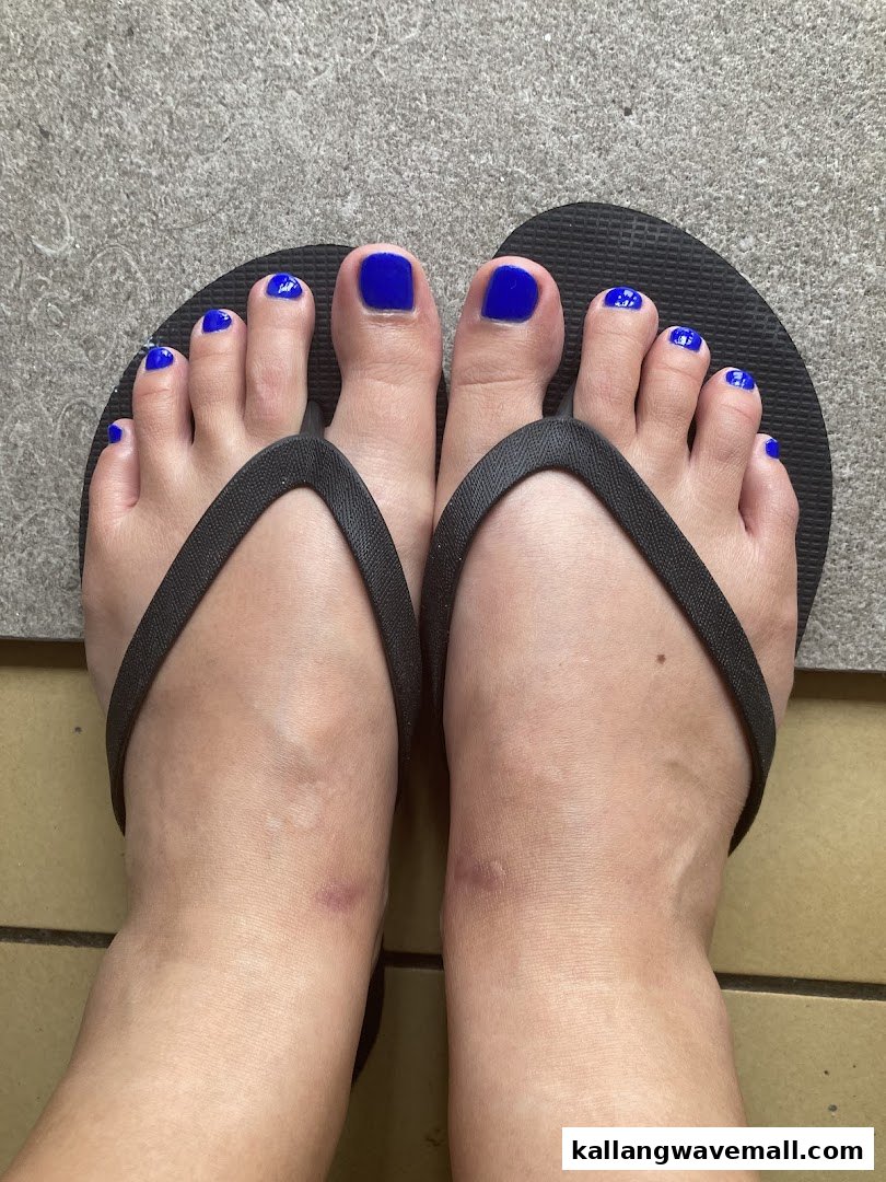 Close-up of feet showcasing a vibrant blue pedicure with black flip-flops on a tiled floor.