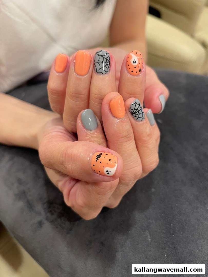 Close-up of hands showcasing Halloween-themed nail art with orange, grey, spiderweb, and ghost designs.