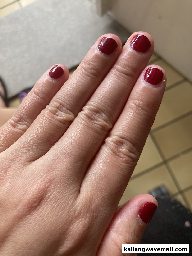 A close-up of a hand showcasing freshly painted dark red fingernails, highlighting a beauty service.