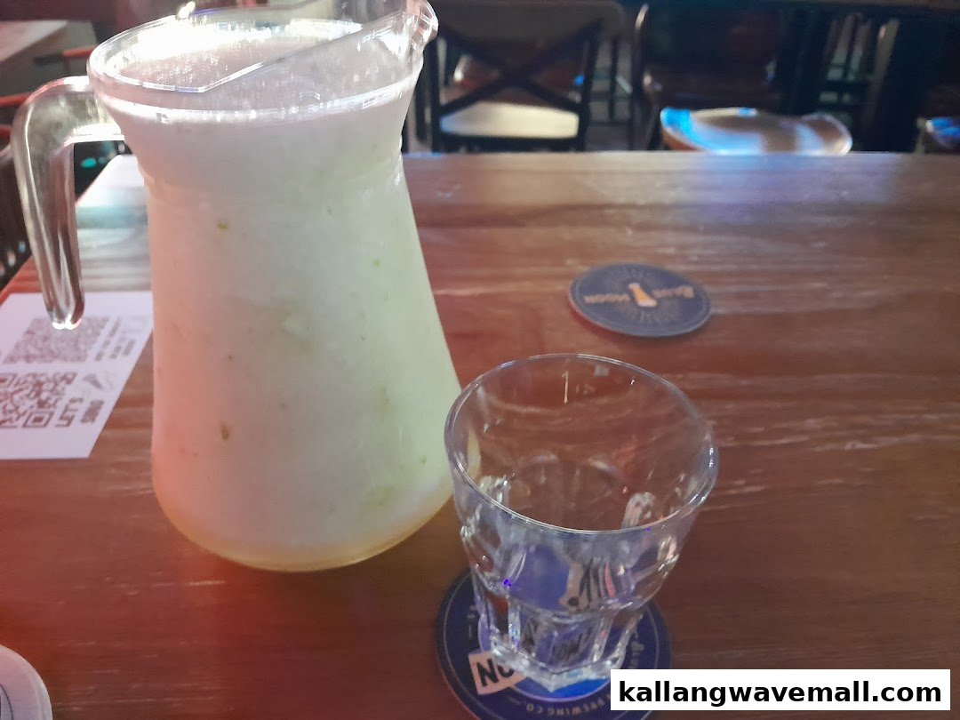 A pitcher of a refreshing light-colored drink and an empty glass on a wooden table in a bar setting.