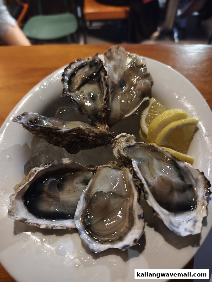 A plate of fresh oysters on ice with lemon wedges, served on a white dish.