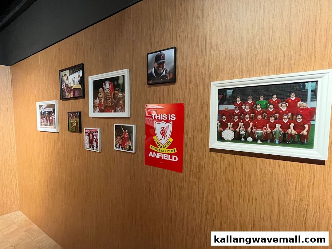 A wooden wall adorned with framed Liverpool FC photos and a 'This is Anfield' poster.