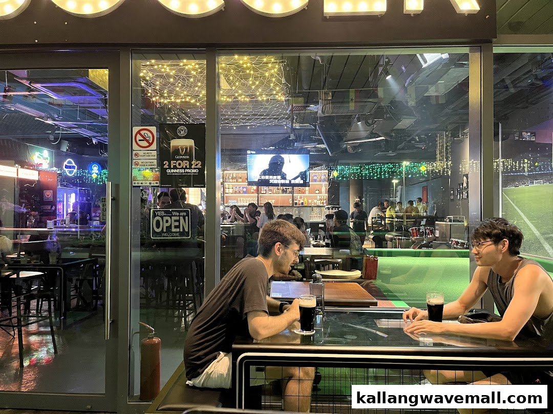 Two men enjoy drinks inside Bar Soccer, a lively sports bar with large screens.
