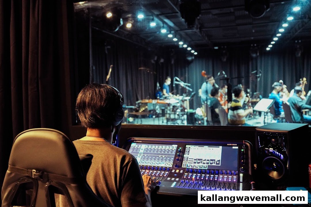 A sound engineer operates a mixing console, overseeing musicians in a recording studio or performance space.