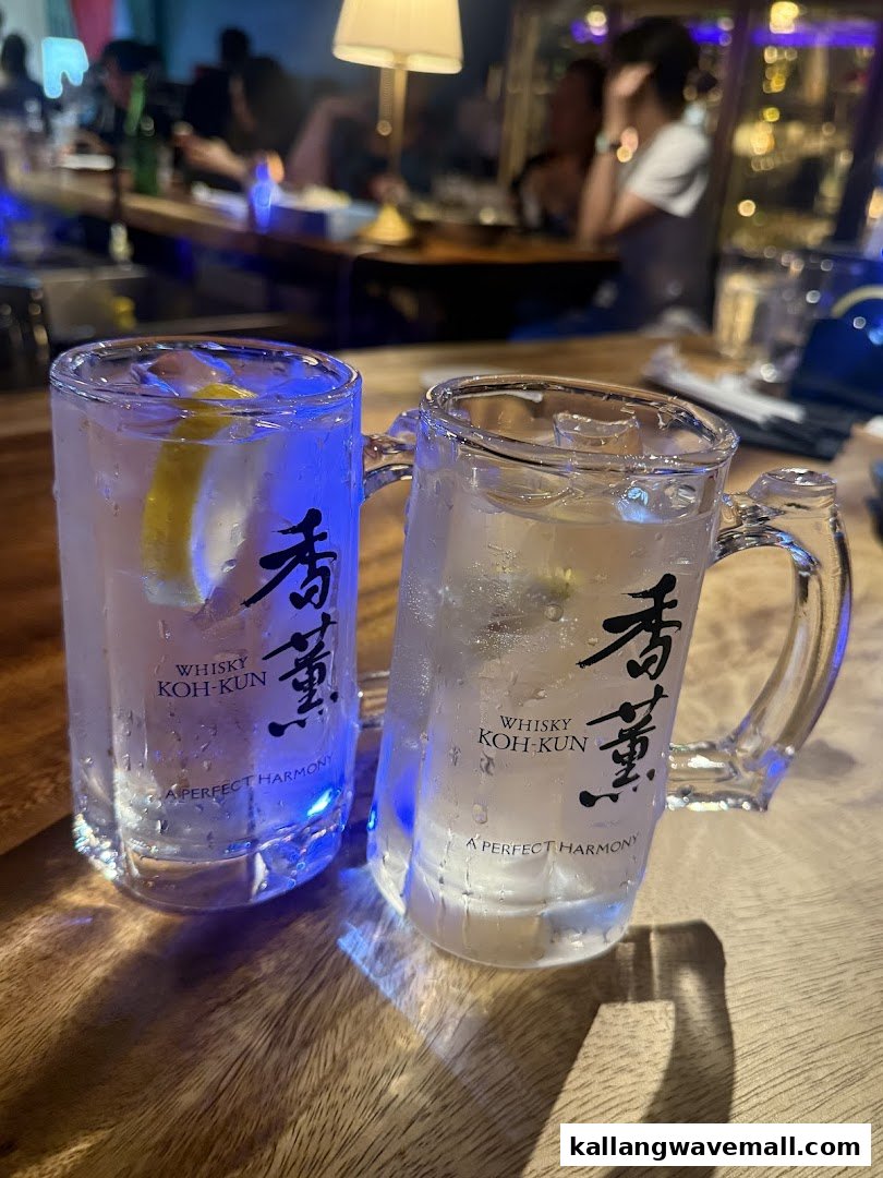 Two refreshing whisky highball drinks with lemon on a wooden bar counter in a dimly lit setting.