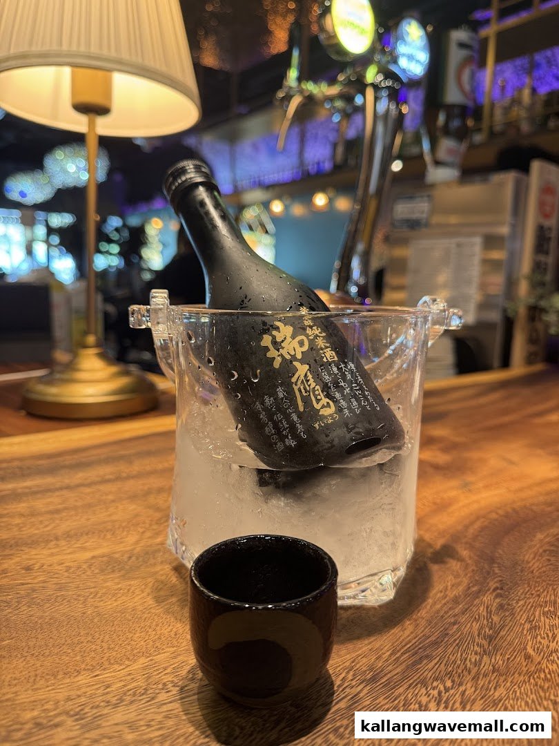 A bottle of sake in an ice bucket with a cup on a wooden bar at a restaurant.