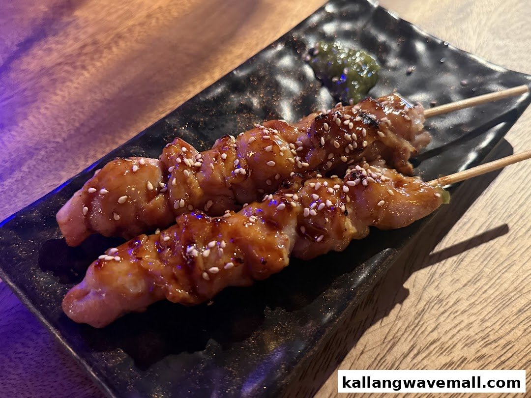 Two skewers of glazed grilled meat with sesame seeds on a black rectangular plate.