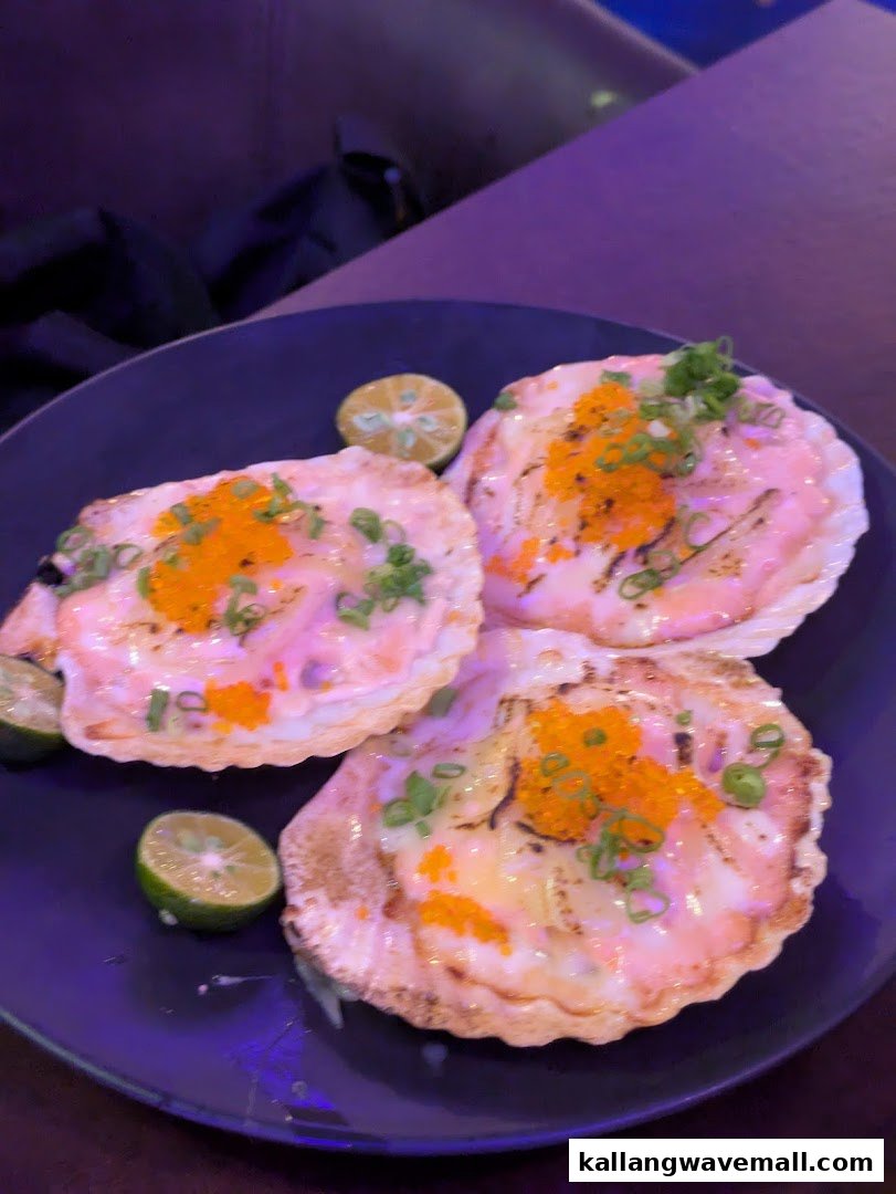 Three baked scallops topped with roe and green onions, served with lime wedges on a dark plate.