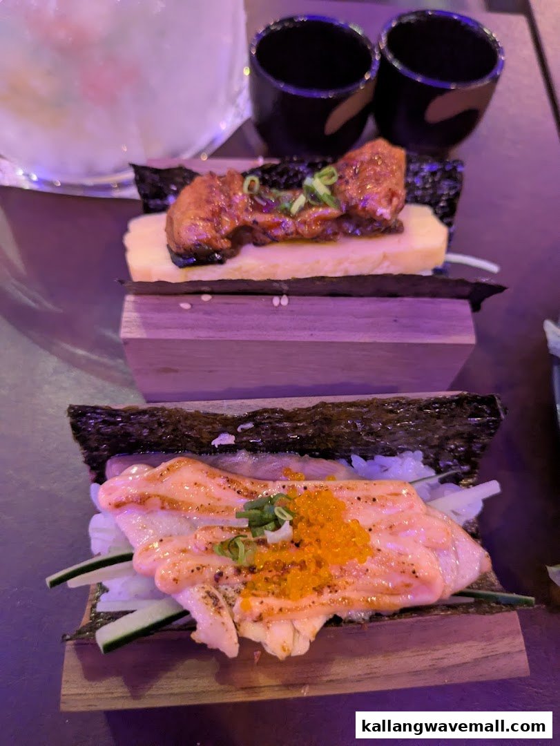 Two artfully presented sushi or hand roll dishes on wooden stands, with sake cups in the background.