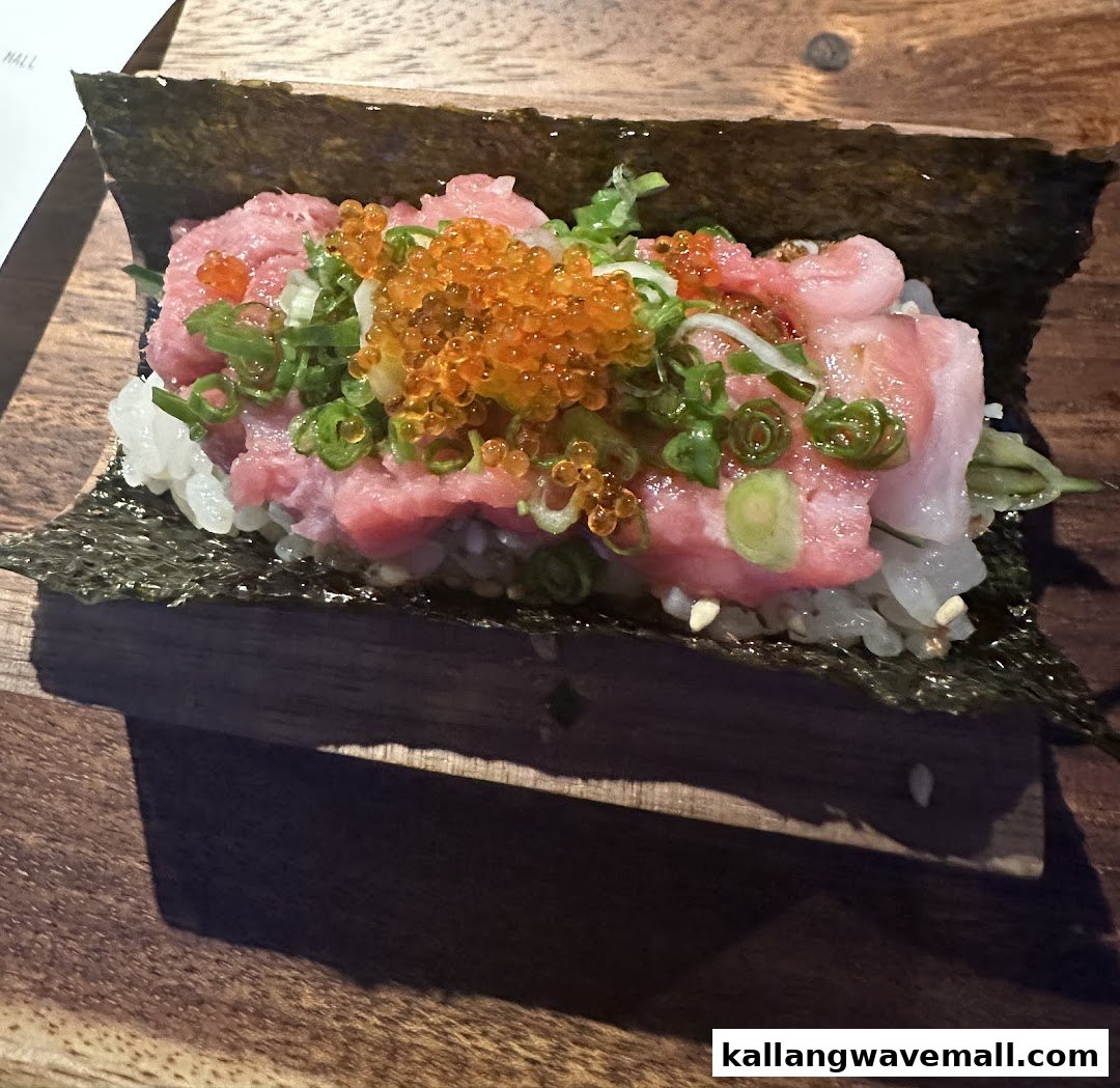 A vibrant sushi roll featuring fresh tuna, bright orange roe, and green onions on a wooden surface.