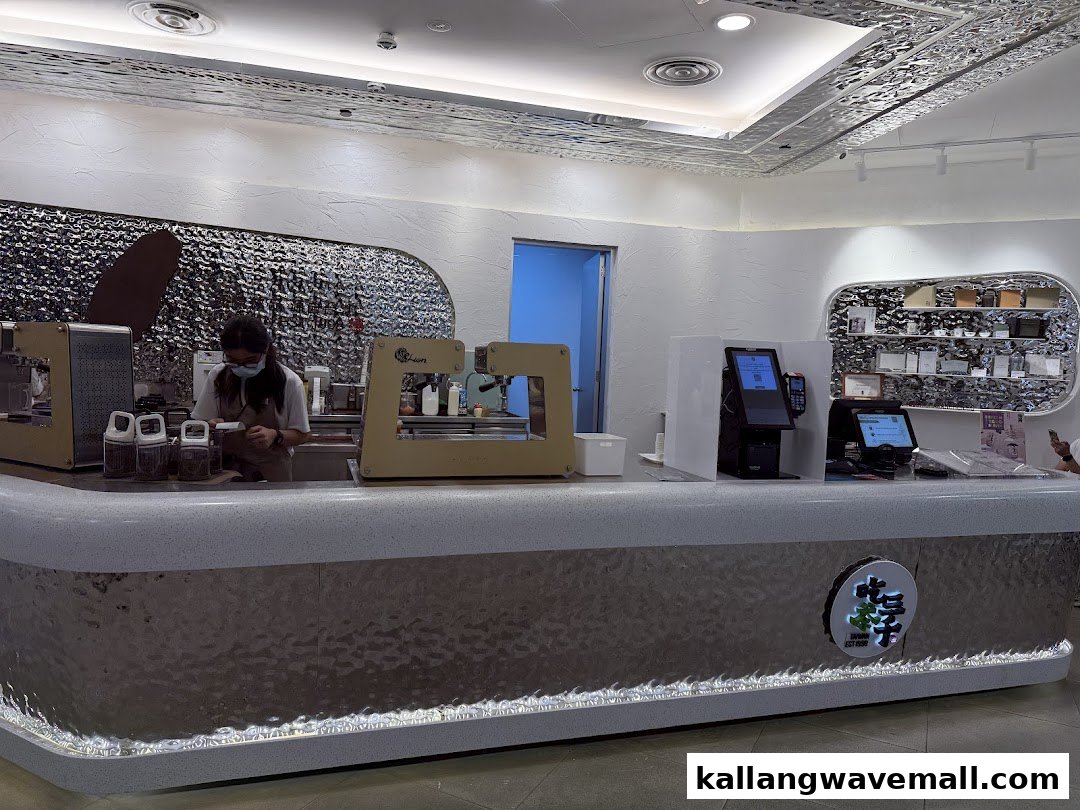 An interior view of CHICHA San Chen's modern counter with a staff member and ordering kiosks.