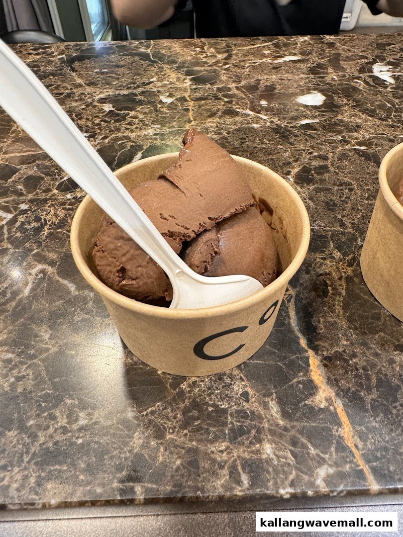 A cup of rich chocolate ice cream with a spoon on a marble counter.