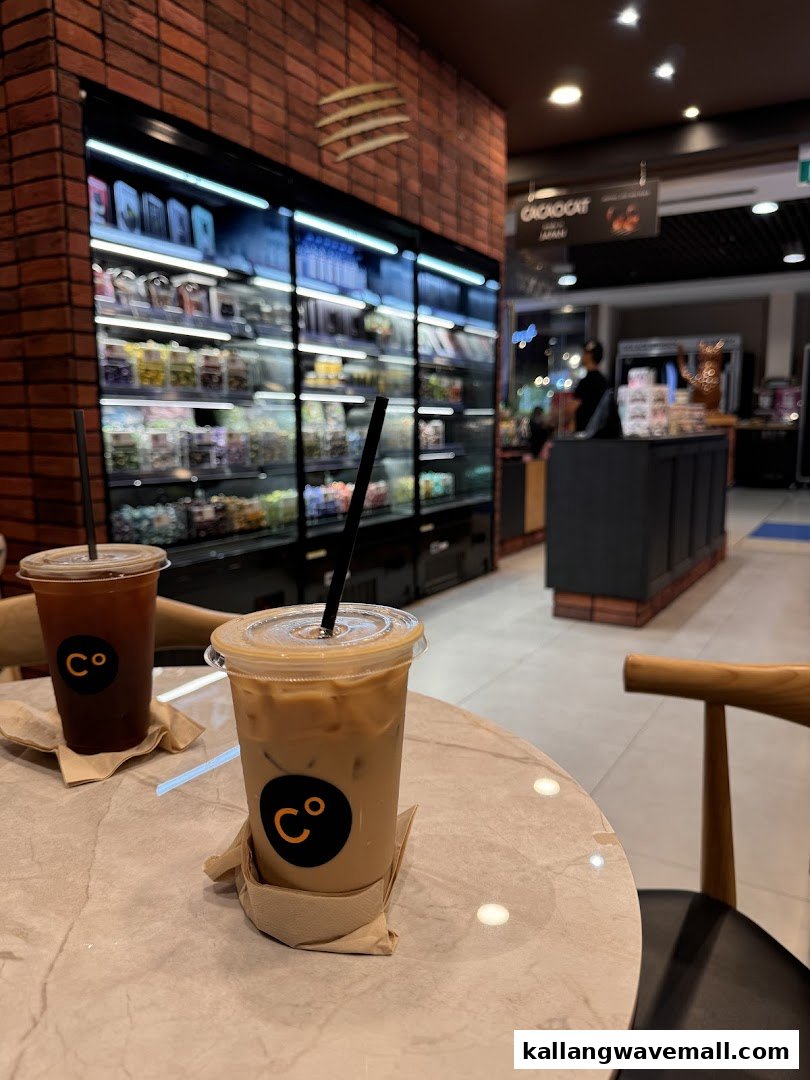 Two iced beverages on a marble table inside Chocolate Origin, with a display case and counter in the background.