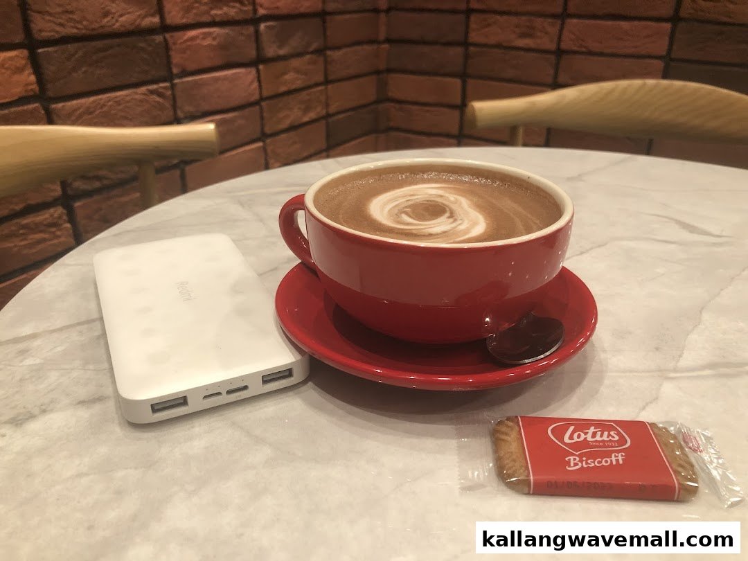A red cup of hot chocolate with a Biscoff cookie and power bank on a marble table.