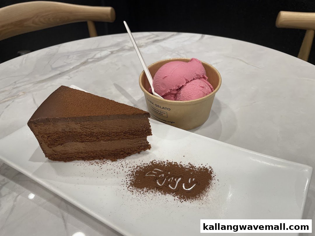 A slice of rich chocolate cake and a cup of pink gelato on a white table.
