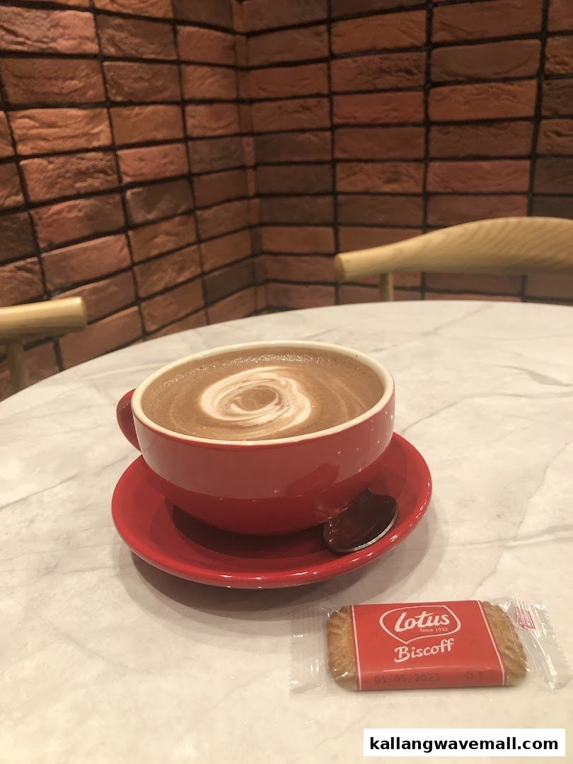 A red cup of hot chocolate with latte art and a Lotus Biscoff biscuit on a marble table.