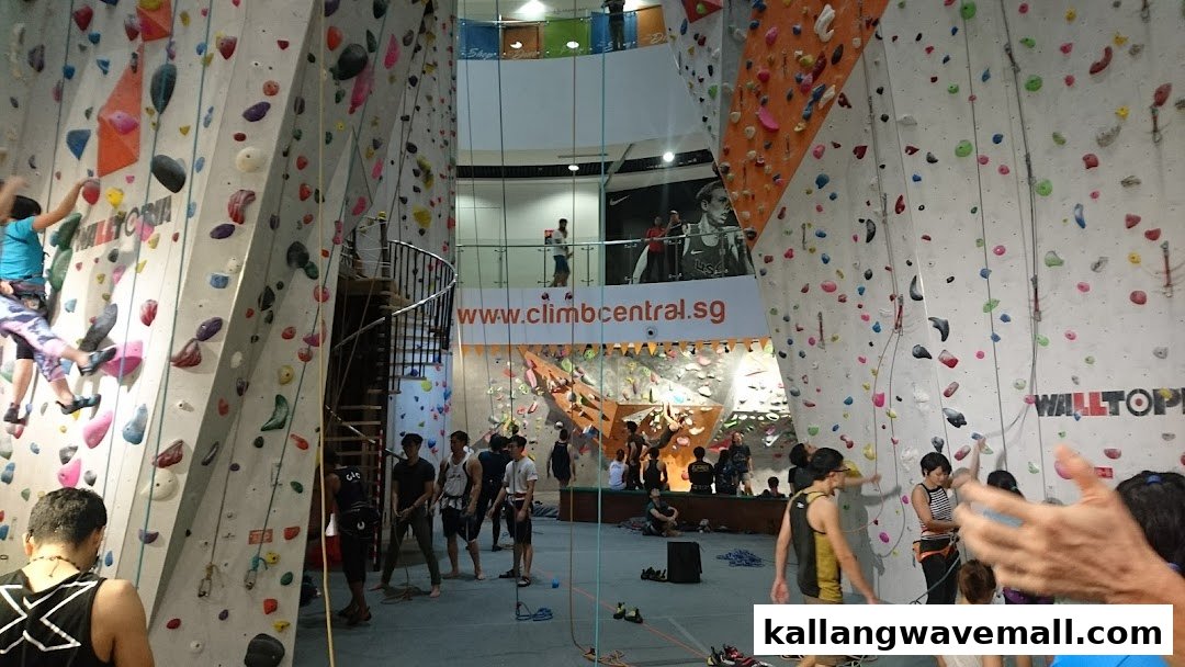 An indoor climbing gym with multiple colorful climbing walls, featuring climbers and people on the ground.