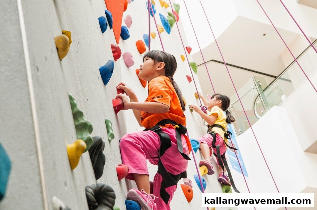 Two young girls actively climbing an indoor rock wall with colorful holds and safety ropes.